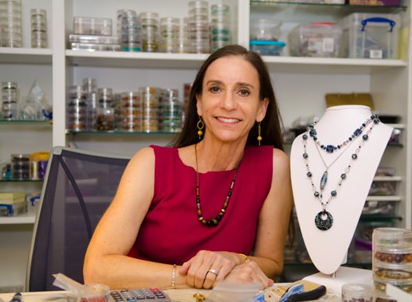 Jewelry designer sitting beside necklace display.