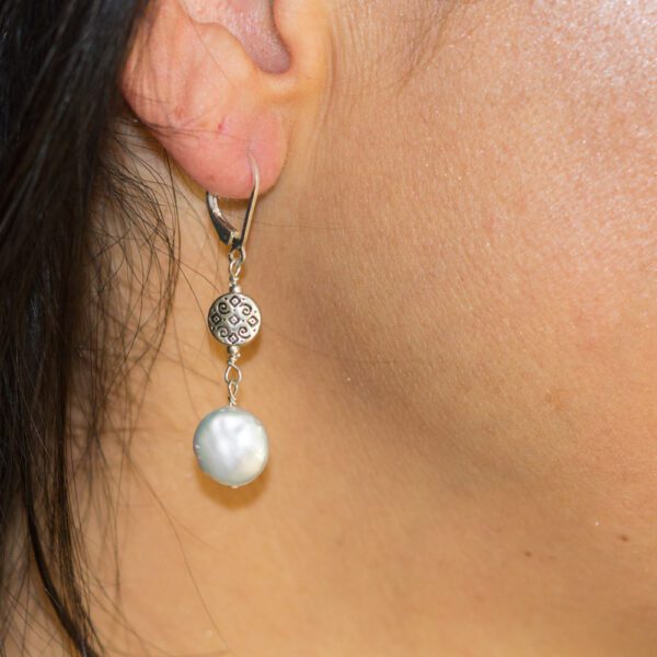 A woman wearing earrings with pearls hanging from them.