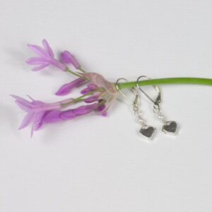 A pair of silver heart earrings sitting on top of purple flowers.