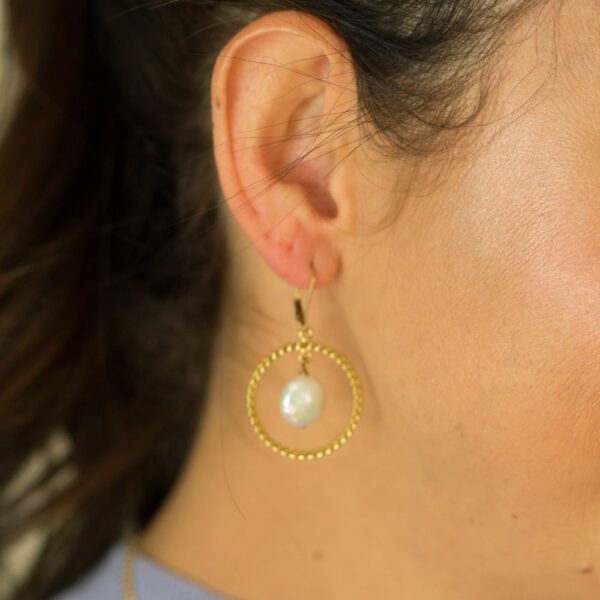 A woman wearing gold earrings with pearls.