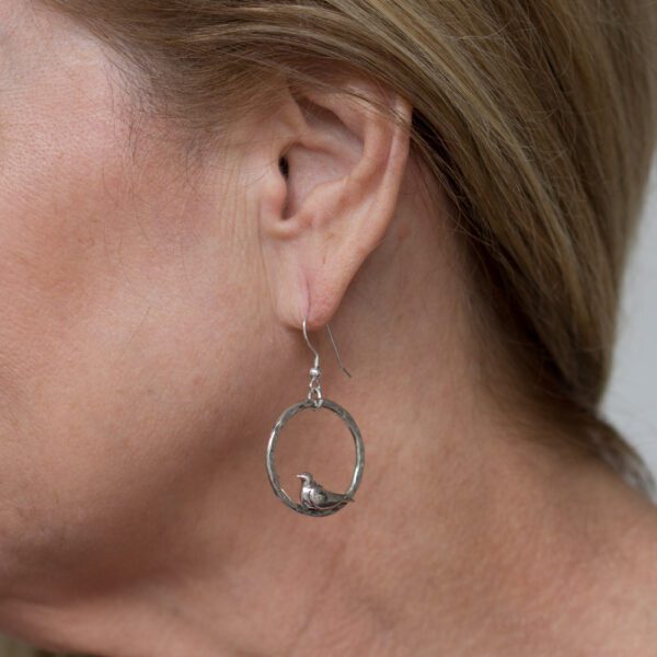 A woman wearing silver earrings with a bird on it.