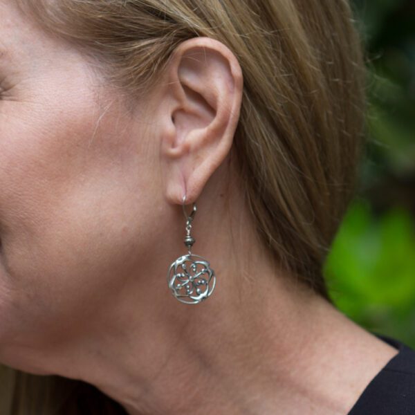 A woman wearing earrings with a tree of life design.