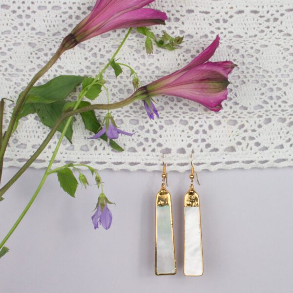 A pair of earrings hanging on the wall next to flowers.