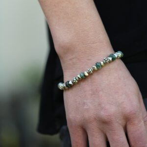 A woman wearing gold and green beaded bracelet