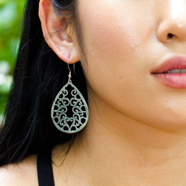 A woman wearing earrings with green and black designs.