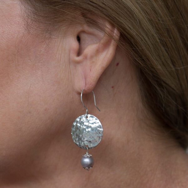 A woman wearing silver earrings with pearls.