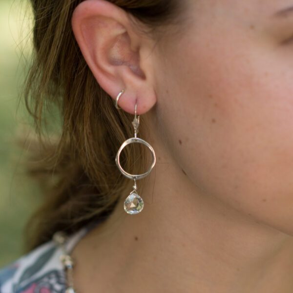 A woman wearing earrings with a glass bead hanging from them.