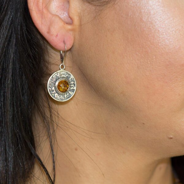 A woman wearing earrings with an orange stone.