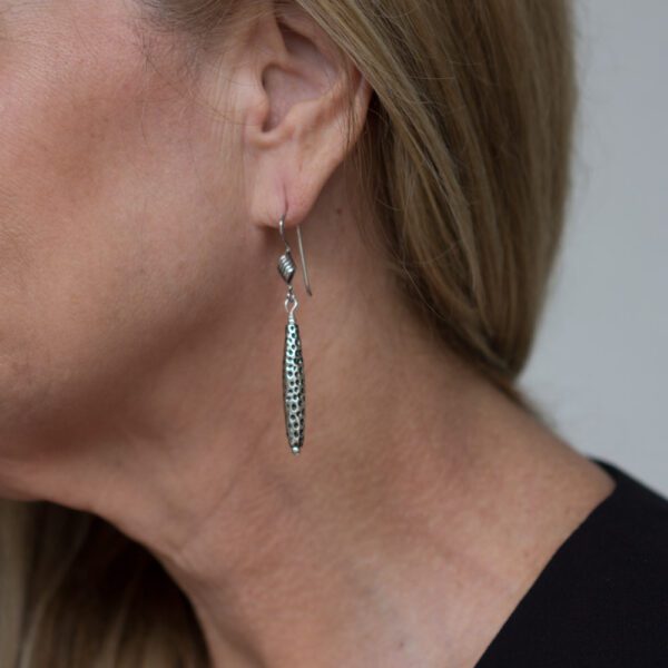 A woman wearing silver earrings with long dangling design.