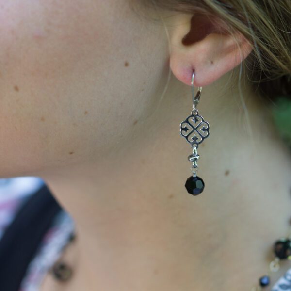 A woman wearing earrings with black beads hanging from them.