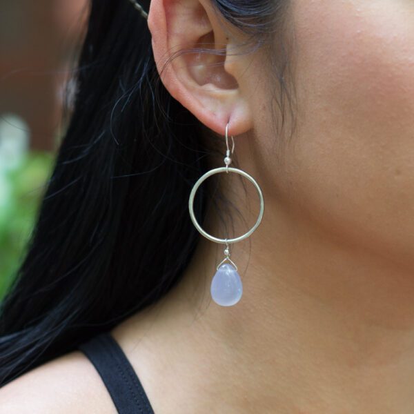 A woman wearing earrings with a blue stone hanging from them.