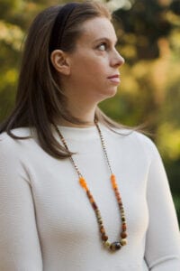 A woman wearing an orange necklace and white shirt.