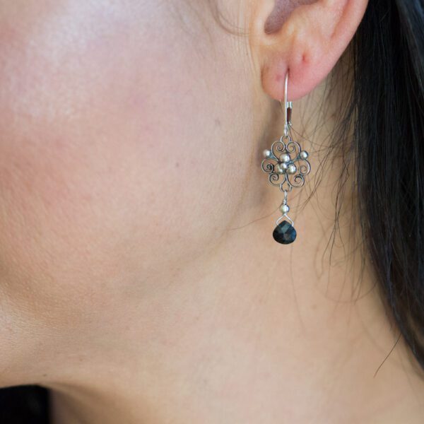 A woman wearing earrings with black stones hanging from them.