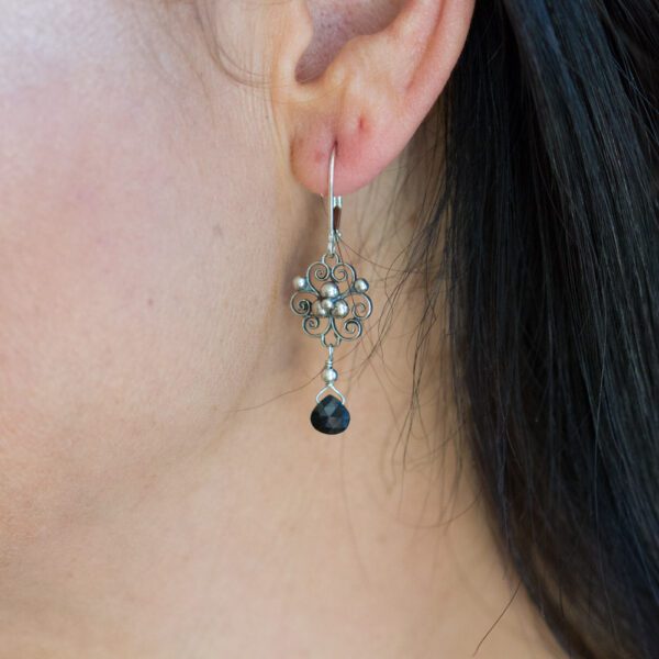 A woman wearing earrings with black stones hanging from them.