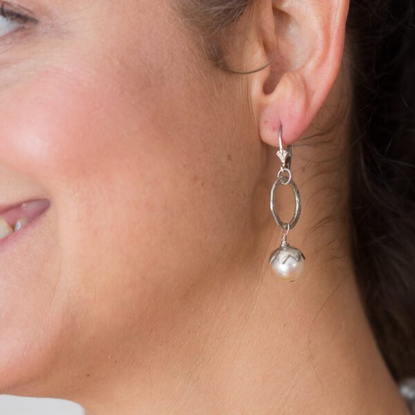 A woman wearing silver earrings with a white pearl.