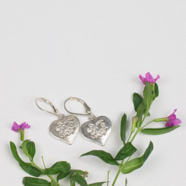 A pair of silver earrings sitting next to purple flowers.