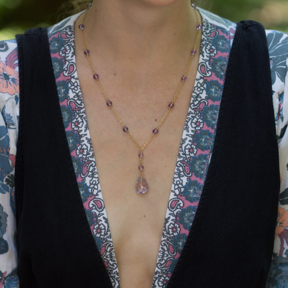 A woman wearing a necklace with amethyst stones and gold chain.