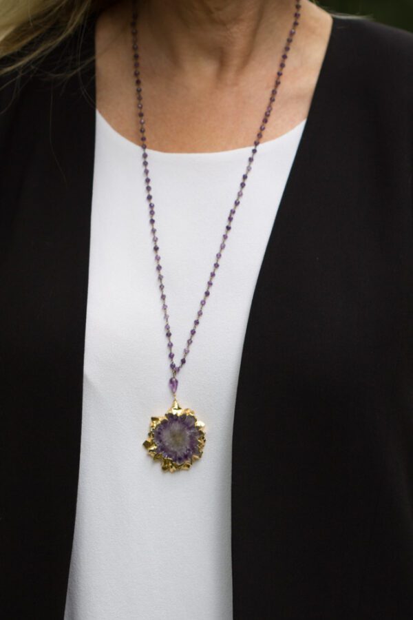 A person wearing a necklace with a purple flower on it.