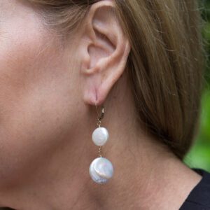 A woman wearing earrings with two pearls hanging from them.