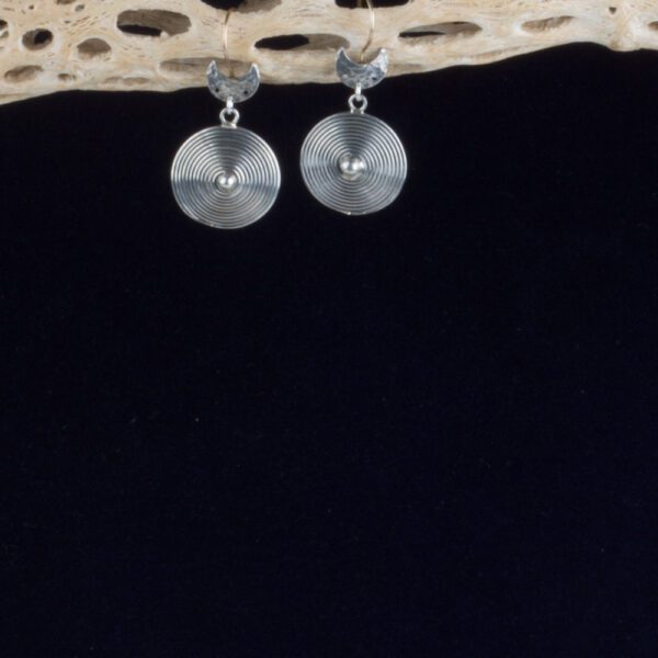 A pair of silver earrings hanging on top of a wooden table.