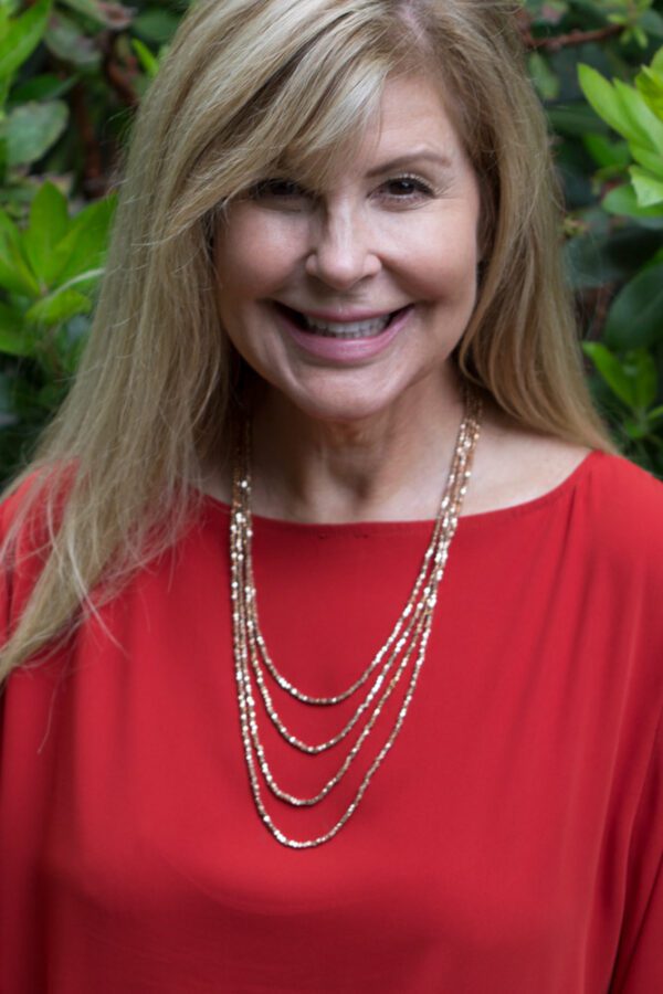 A woman wearing a red top and gold necklace.