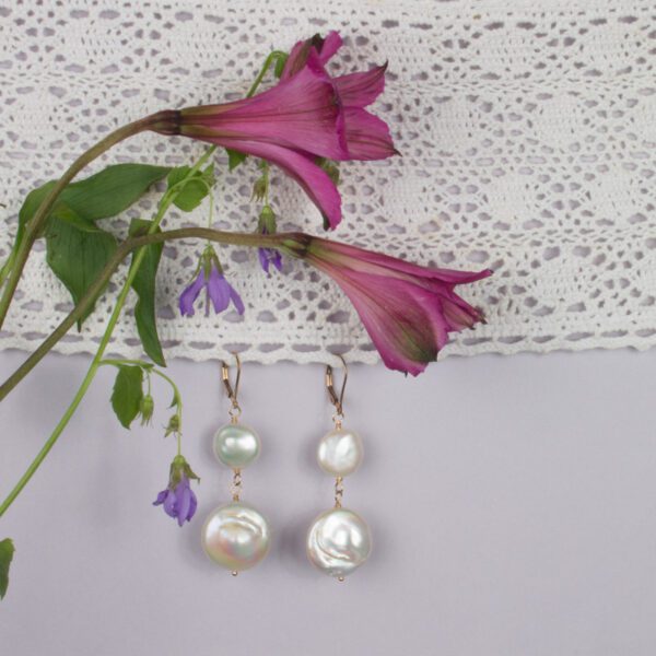 A pair of earrings hanging on the wall next to flowers.