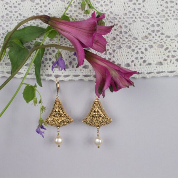 A pair of gold earrings hanging on top of a lace curtain.