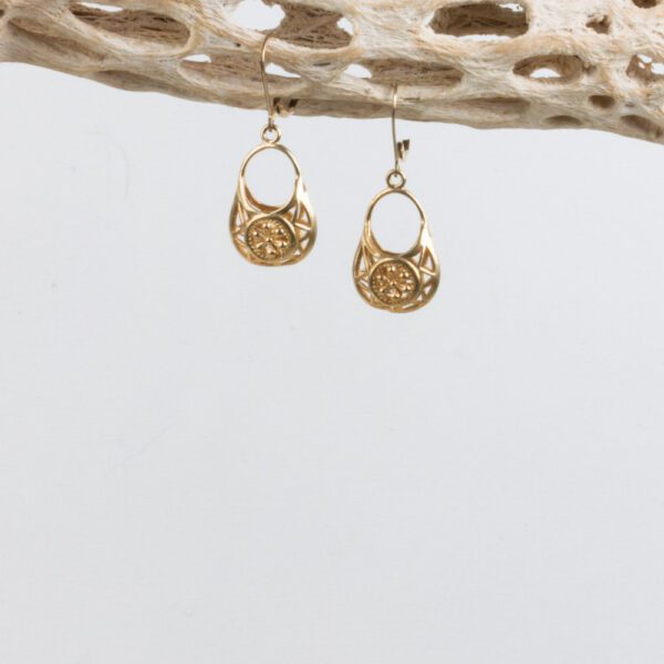 A pair of gold earrings hanging from a wooden structure.