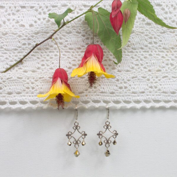 A pair of earrings hanging on the side of a white lace curtain.