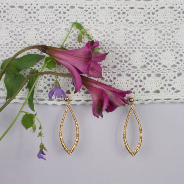 A purple flower and some gold earrings hanging on the wall