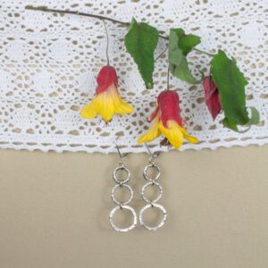 A pair of silver earrings hanging on a white lace doily.