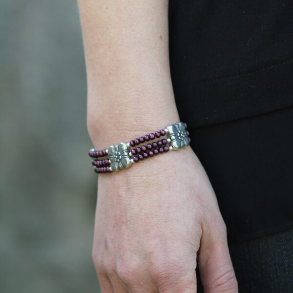 A woman wearing a bracelet with three rows of garnet colored pearls