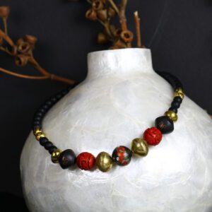 A white vase with a black and red necklace.