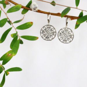 A pair of silver earrings hanging from a tree branch.