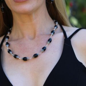 A woman wearing black and white beads in front of trees.