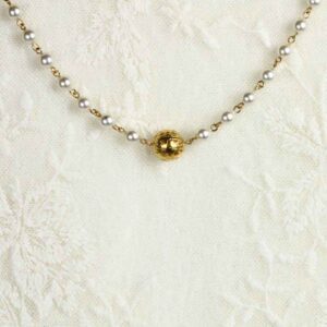 A gold bead and pearl necklace on a white lace background